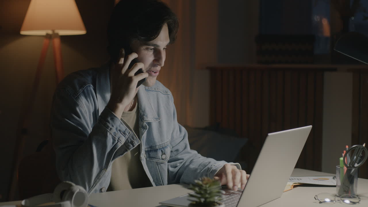 Man working on laptop and talking on the phone at night