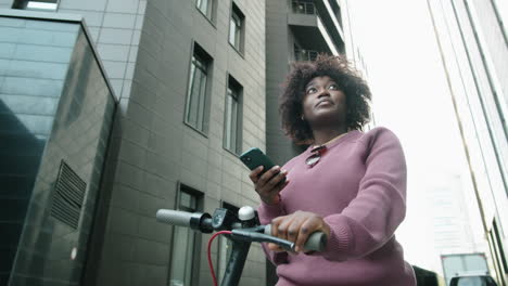 Afroamerikanische-Frau-Steht-Mit-E-Scooter-In-Der-Stadt-Und-Benutzt-Smartphone