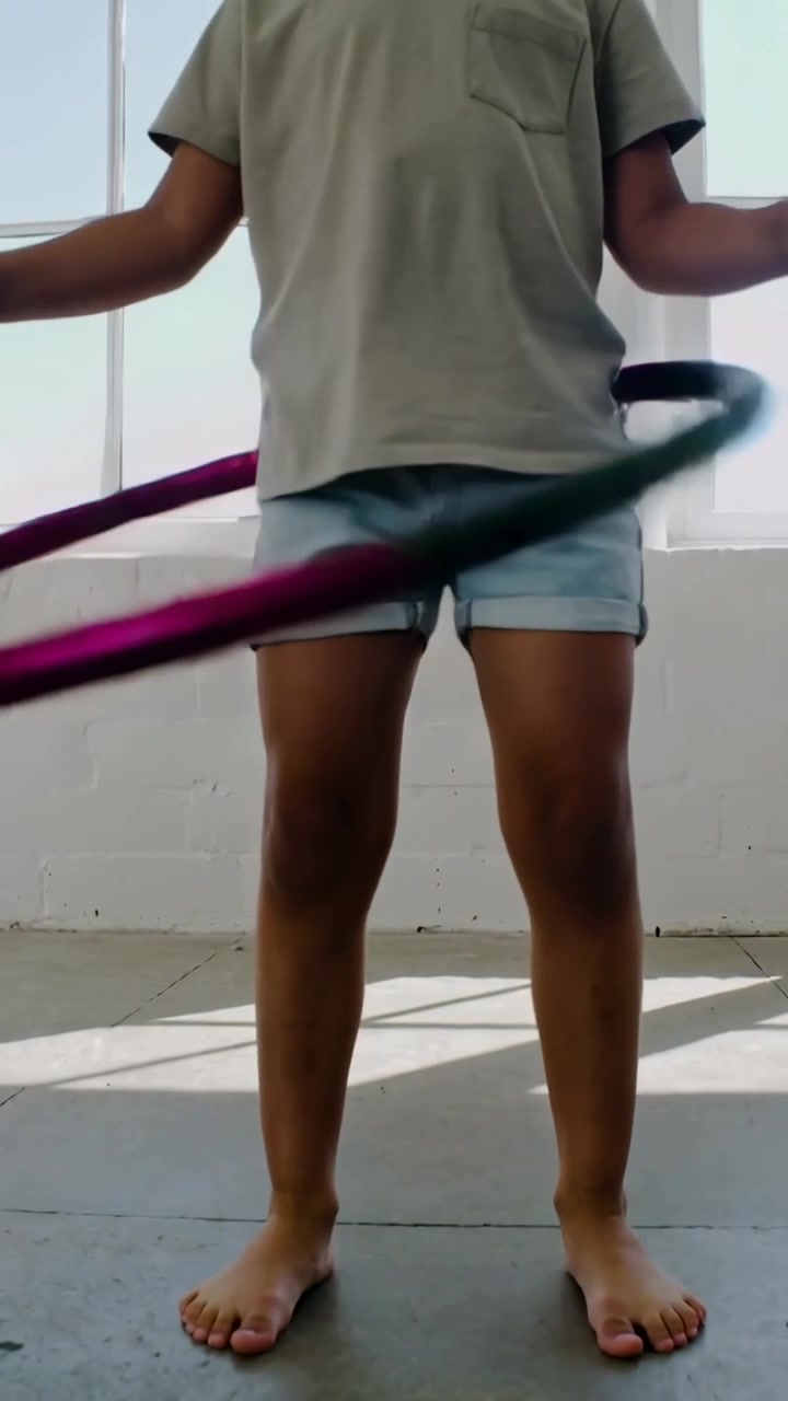 Vertical video: Spinning child mid-hoop, rotating hips, keeping hoop moving before large window