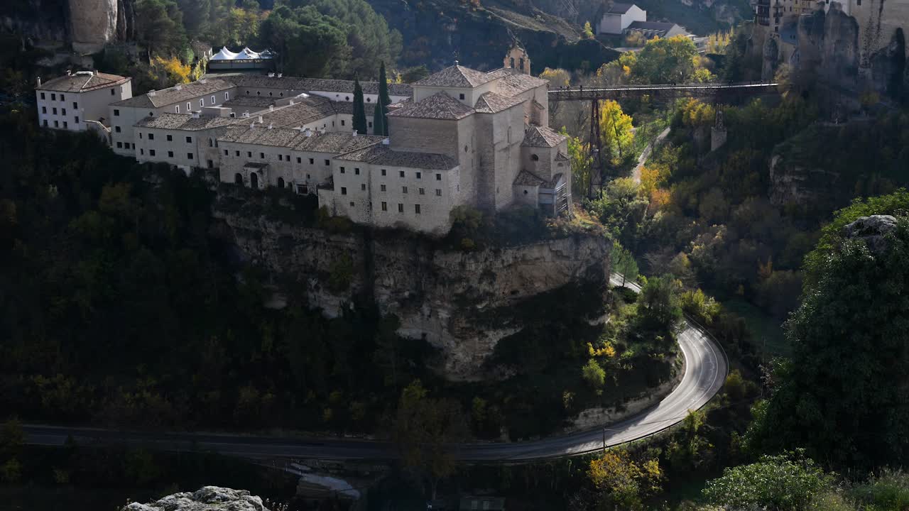 CUENCA, SPAIN - A high-angle aerial shot captures the historic Parador hotel, a former convent, perched on a cliff above the gorge during a vibrant autumn.