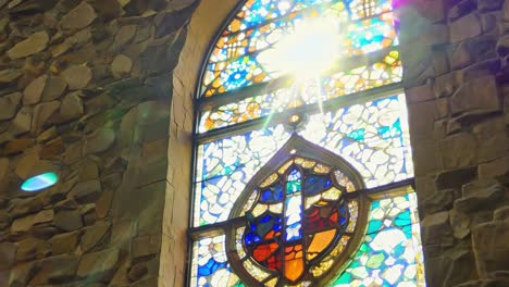 sunlight streaming through a stained glass window illuminates the interior of a stone church, creating a vibrant atmosphere