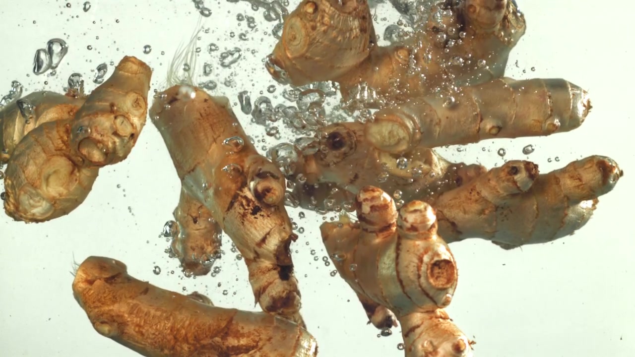 Radici di zenzero fresco che cadono in acqua limpida con bolle