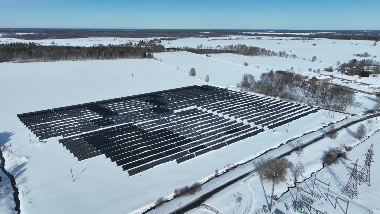 Dron pomalu letí směrem k panelům solární elektrárny v řadě na zasněžených polích. Haljala, Estonsko.