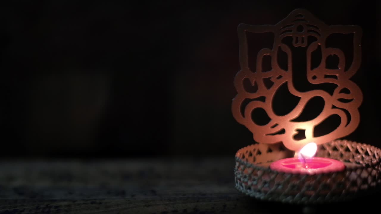 Slow pannning closeup to a Ganesha cutout with tea candle being blown off with smoke and darkness, or Ganapati, Vinayaka, is one of the best-known and most worshipped deities in the Hindu pantheon.