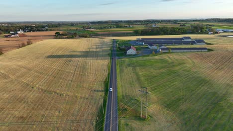 Aerial-view-of-a-rural-landscape-featuring-a-long,-straight-road-flanked-by-vast-golden-fields-and-green-pastures