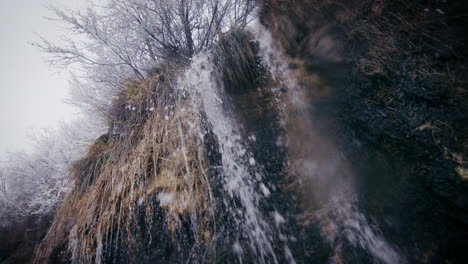 Icy-cold-waterfall,-frost-on-trees-and-grass,-winter-snowy-scenery