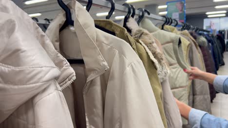 A Woman Chooses Used Jackets on Racks in a Thrift Store. A woman chooses used jackets on racks in a thrift store. The girl chooses used clothes. Poverty. Cheap clothes