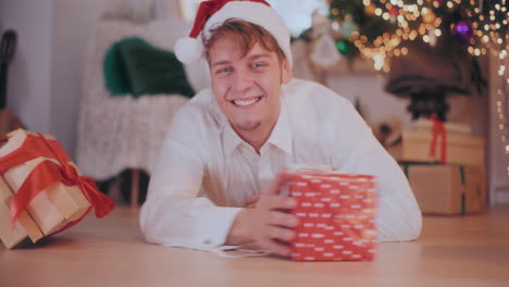 hombre feliz en sombrero de santa deslizando regalos de navidad mientras está tendido en el suelo