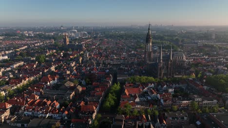 Drone semi orbit over the historic city of Delft, Netherlands, showcasing Nieuwe Kerk tower and surrounding rooftops in golden morning light