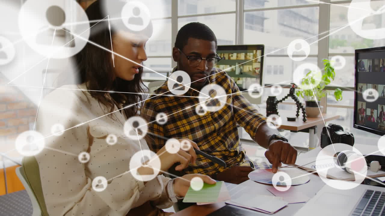Animation of network of profile icons over diverse man and woman discussing over documents at office