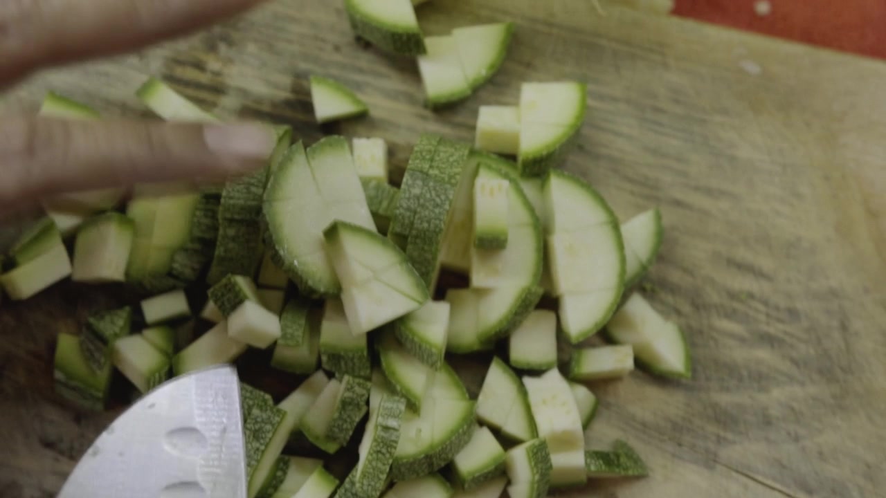 Vista ravvicinata di una mano che taglia pezzi di zucchine fresche con un coltello su un tagliere durante la preparazione di un pasto fatto in casa in cucina.