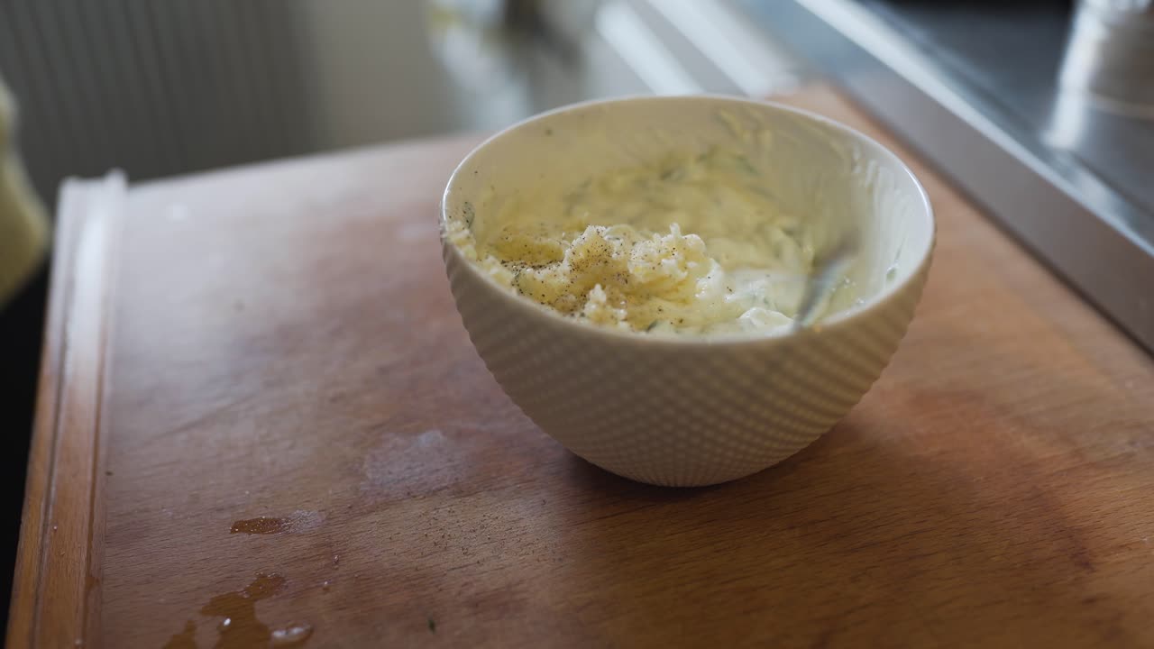 echando sal y pimienta en un bol de tzatziki y mezclando todo junto con una cuchara