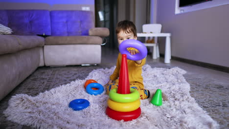 peaceful caucasian kid sitting on soft plaid on the floor. cute toddler assembling pyramid.