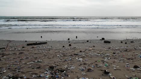 camera moving sideways on a heavily polluted beach, plastic trash washing out from the oceans