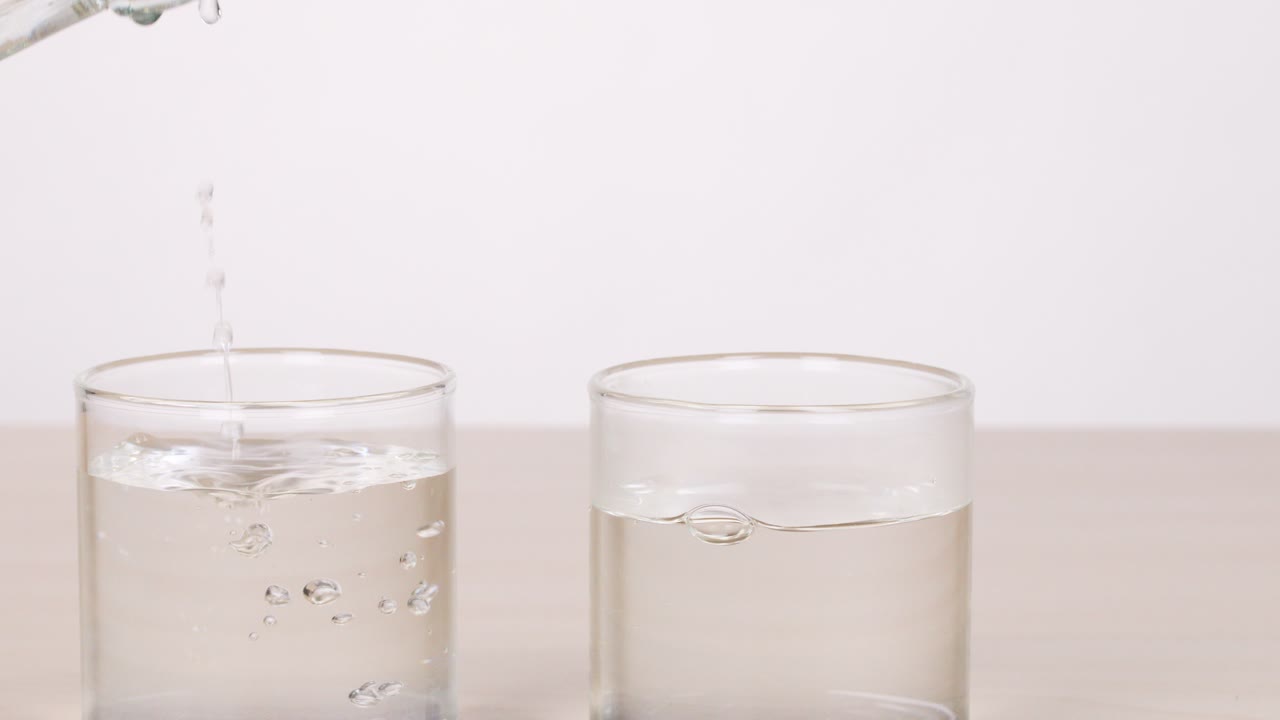 Clear water poured from bottles into two glasses on table, bright lighting, static camera