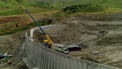 Toma-Aérea-De-Un-Dron-De-Una-Grúa-Trabajando-En-La-Construcción-De-Una-Presa-En-Las-Montañas.