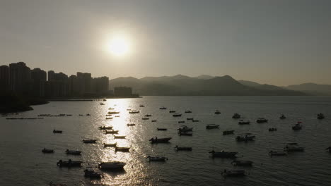 drone shot of bustling port with silhouette of boats at dusk in hong kong, china