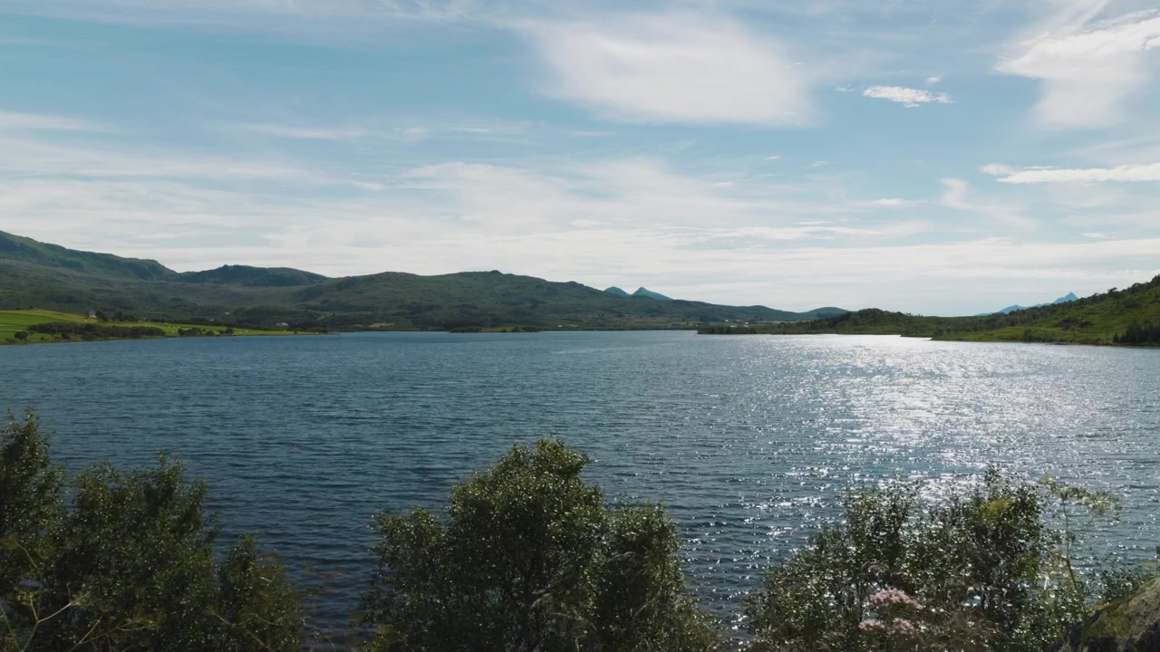 Vista di un lago con paesaggio montano, colline verdi, cielo blu e nuvole nella Norvegia settentrionale, Lofoten.