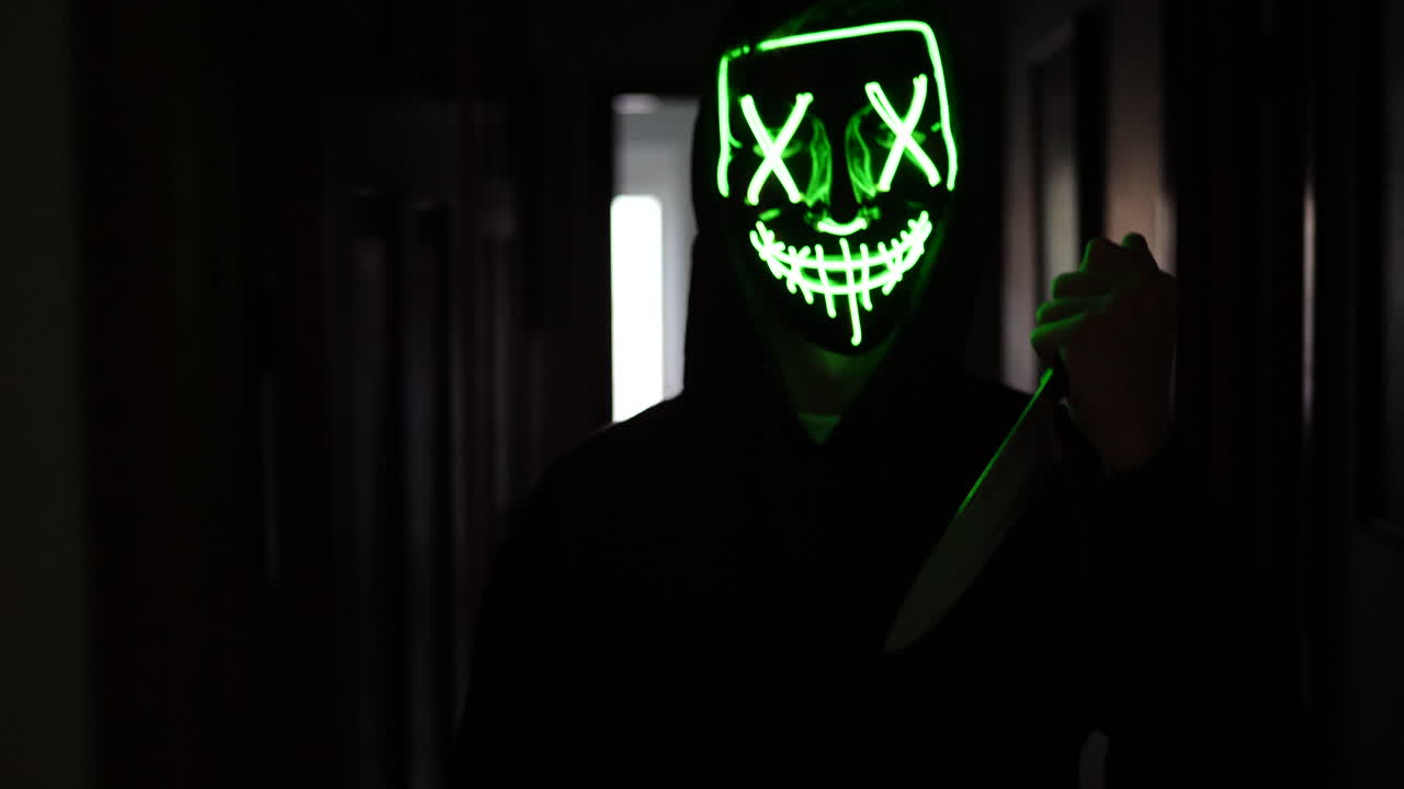 un asesino aterrador con una máscara de halloween anónima genérica que persigue a una víctima asustada con un cuchillo