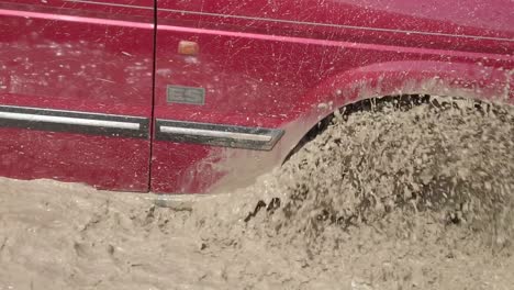 a red vehicle drives through deep muddy waters in slow motion