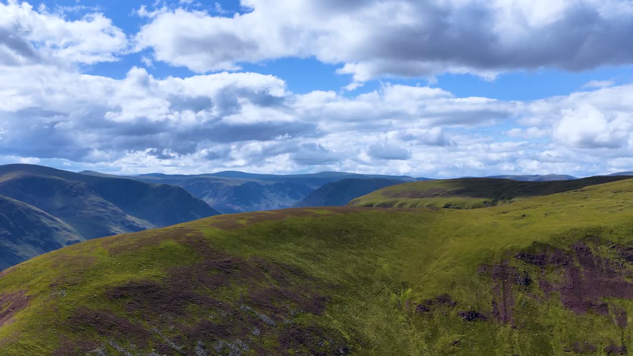 Drone camera smoothly pans across green mountain ridge under dramatic clouds, revealing expansive Highland valleys