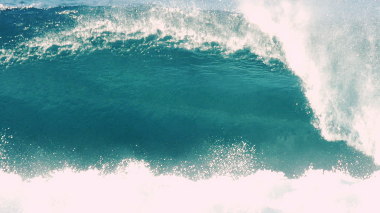 Curling wave crashes over with deep blue tone and soft white foam trails
