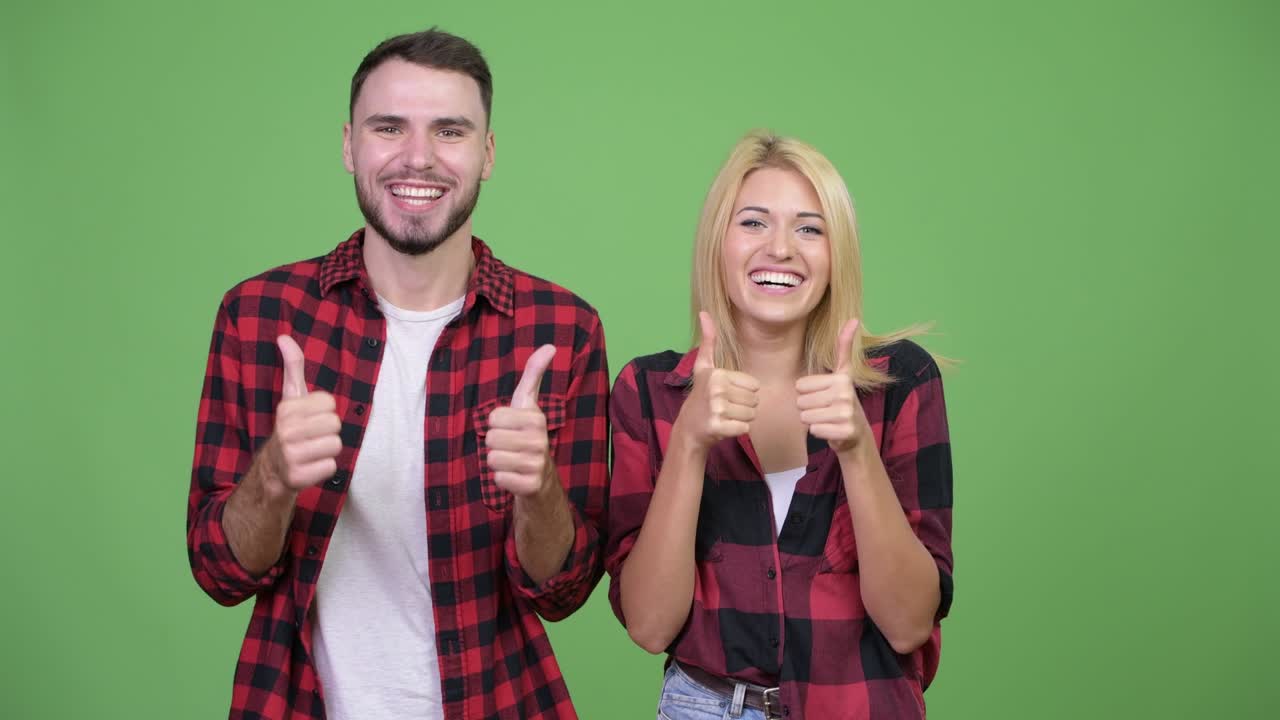 una pareja joven levantando los pulgares juntos.