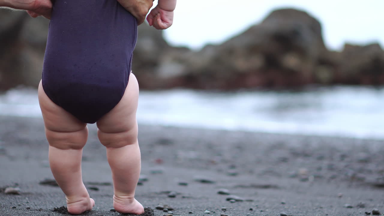 close-up of baby's feet taking their first steps on the black sand on the beach near the ocean