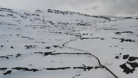 Snowy mountain road in snow covered mountains of iceland. Rocky hills and icy landscape. Aerial view.