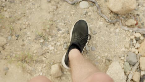 pov closeup shot of man's shoes walking on dry rugged terrain, slow motion