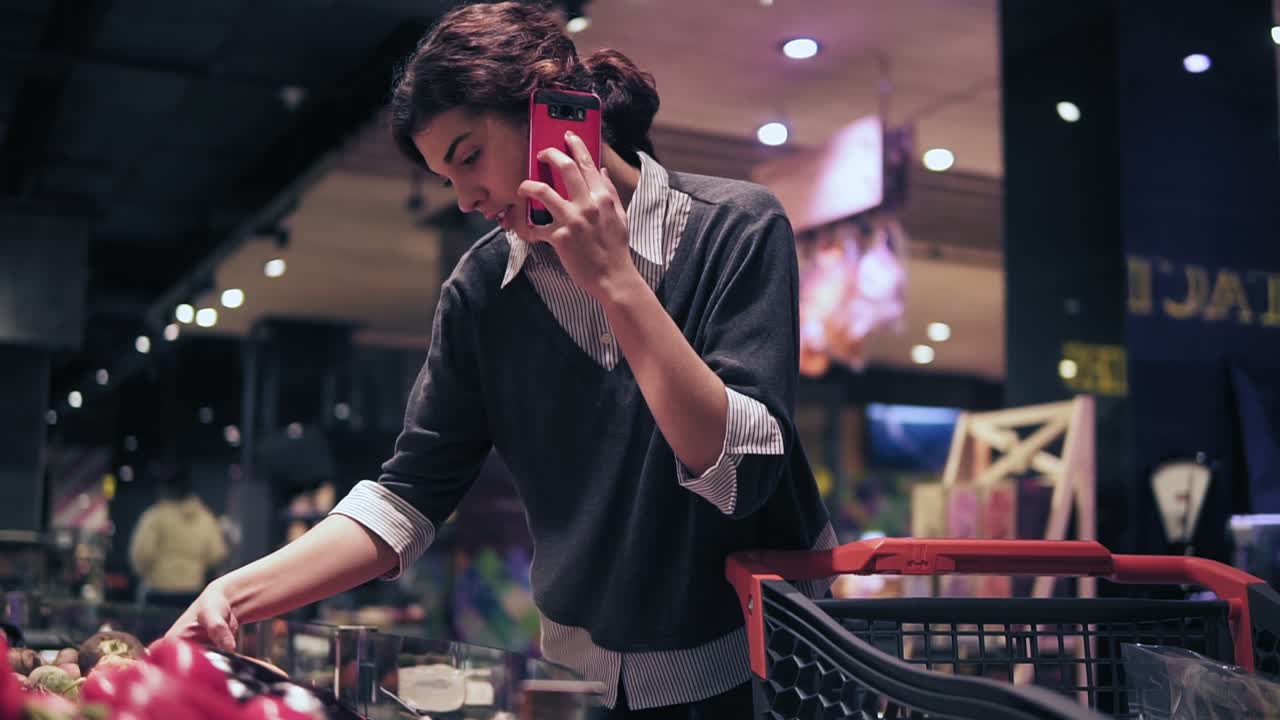Slomo footage of a young female costumer in a grocery store speaking with someone on the phone while picking out carrot.