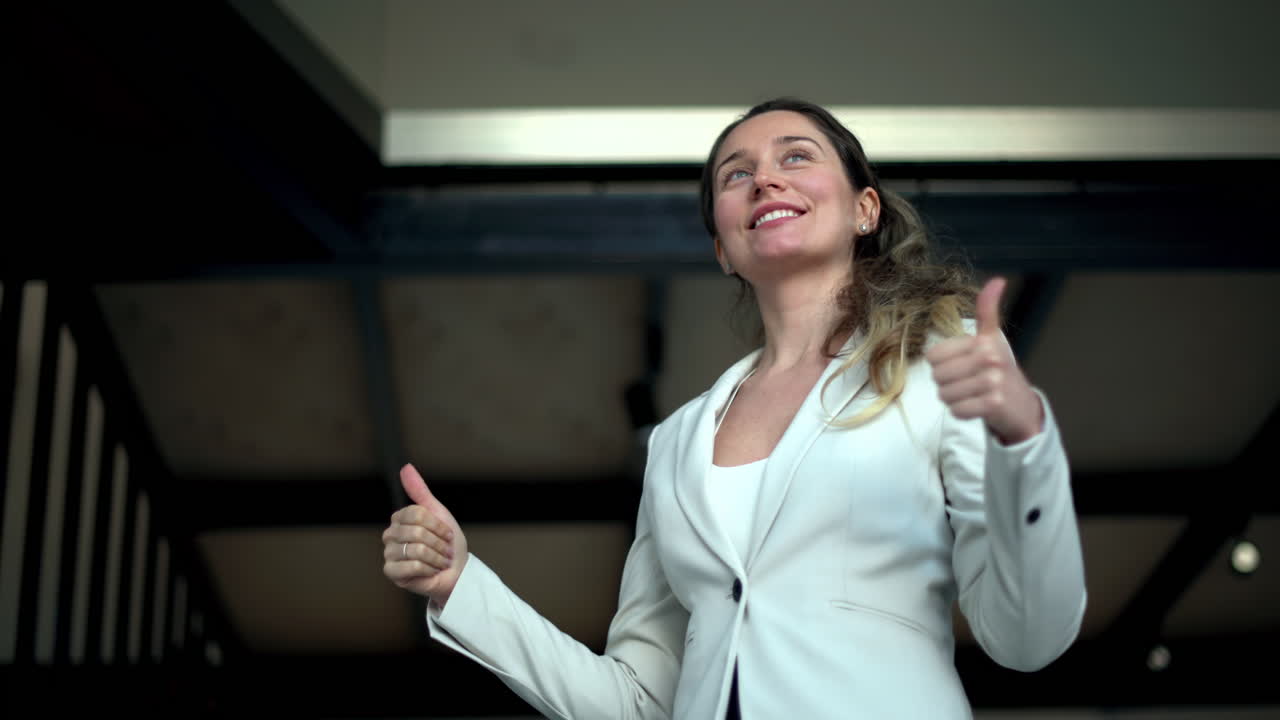 A smiling woman in business attire showing thumbs up gesture, expressing success and optimism