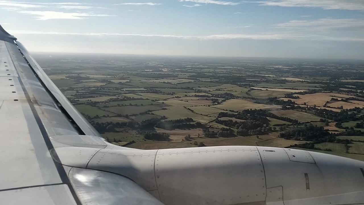 POV shot from airplane window showing wing and aerial view of rural fields and farmlands during descent in clear weather