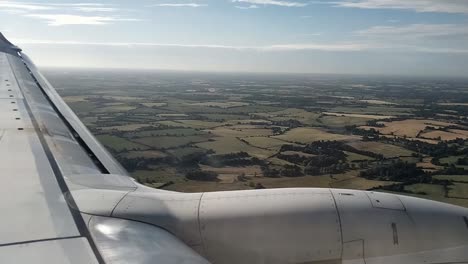 pov shot from airplane window showing wing and aerial view of rural fields and farmlands during descent in clear weather