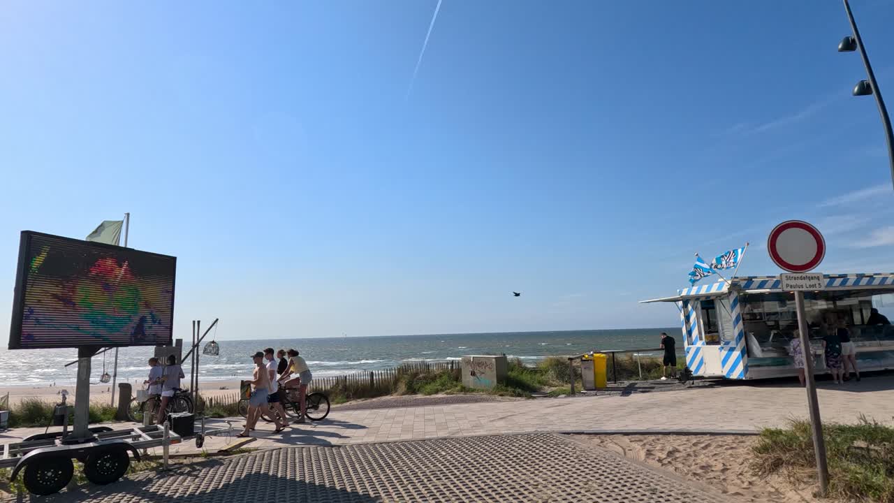 Groups walk and relax by the seaside, bicycles parked, bright daylight, smooth camera pan