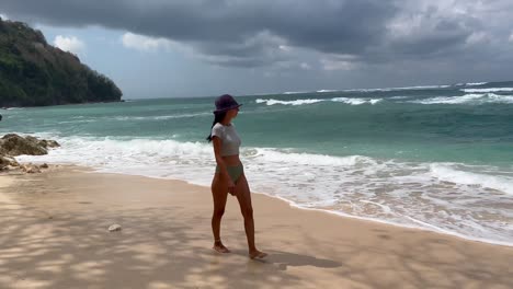 Tranquil-Paradise:-Young-Girl-in-Bikini-Walks-Barefoot-on-Secluded-Green-Bowl-Beach,-Bali