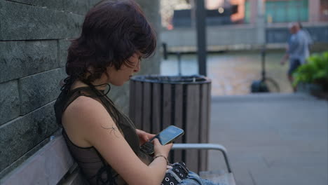 Outdoor-Fashion-Portrait-Of-Young-Alternative-Style-Woman-With-Tattoos-Sitting-On-Bench-Using-Mobile-Phone-1