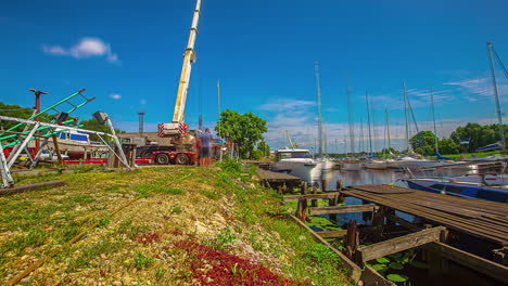 workers and crane lifting up and putting down boat in harbor water