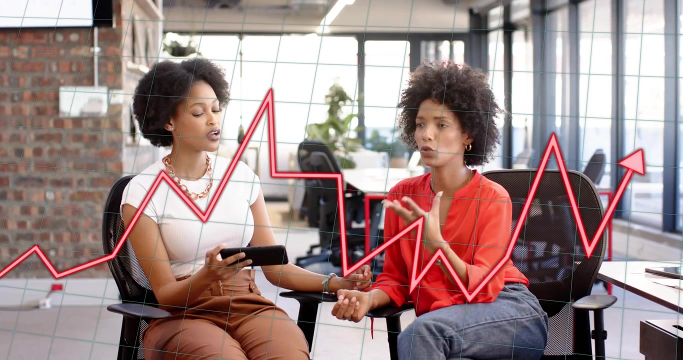 Woman turning tablet toward colleague and analyzing business trends with red line chart fluctuating