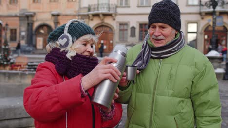 senior wife husband tourists drinking from thermos, enjoying hot drink tea on city central street