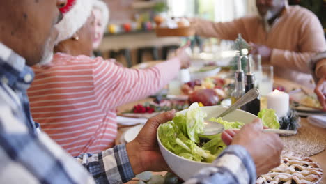 Happy-diverse-senior-male-and-female-friends-serving-food-at-christmas-dinner-table,-slow-motion