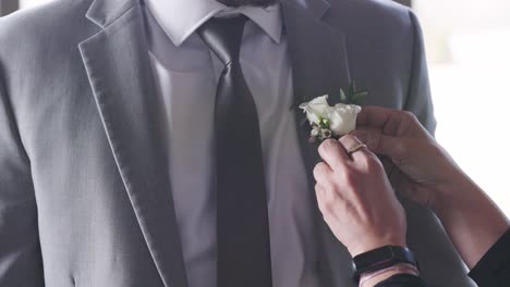 Woman-Attaching-White-Boutonnière-onto-Groom-Grey-Tuxedo