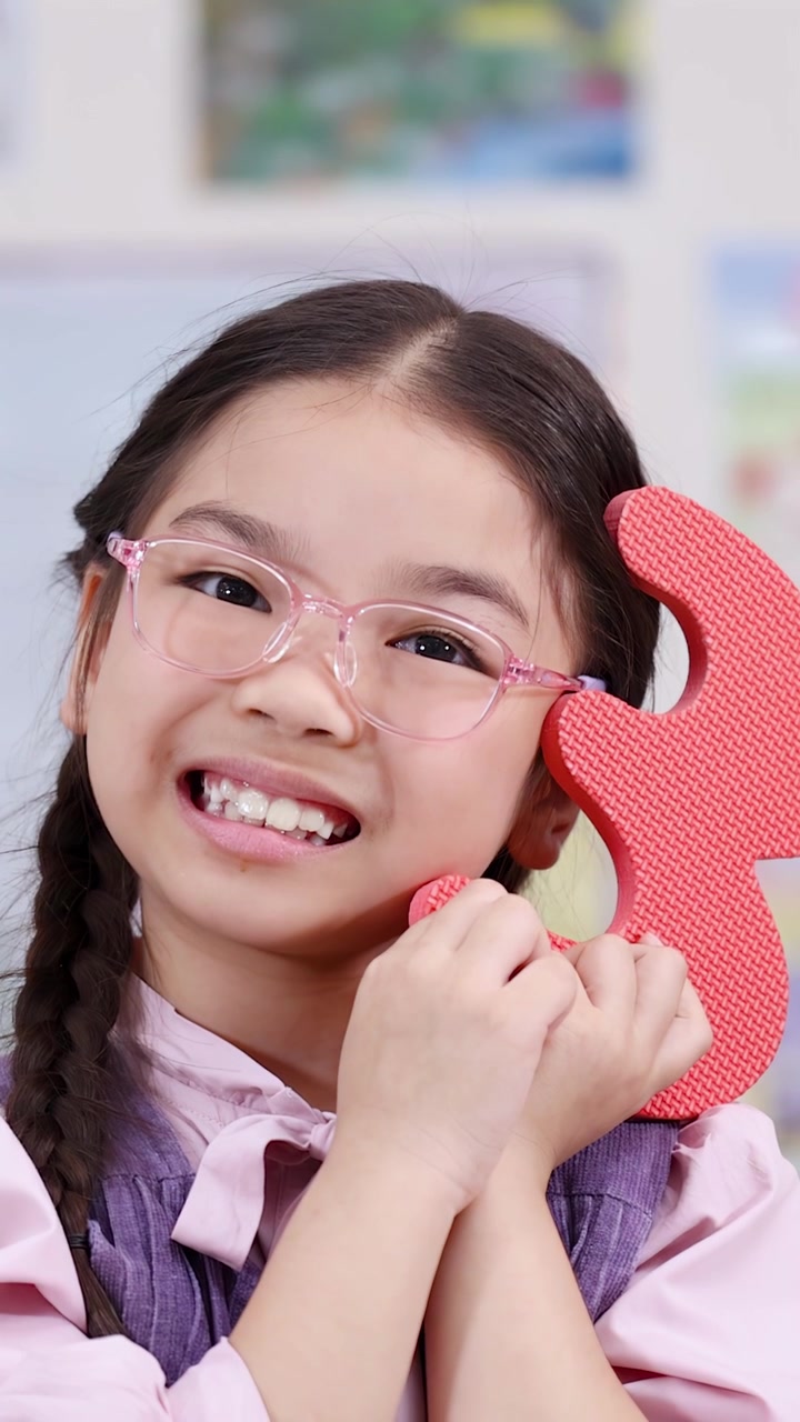 A happy young girl with glasses holds a foam number three during a classroom activity