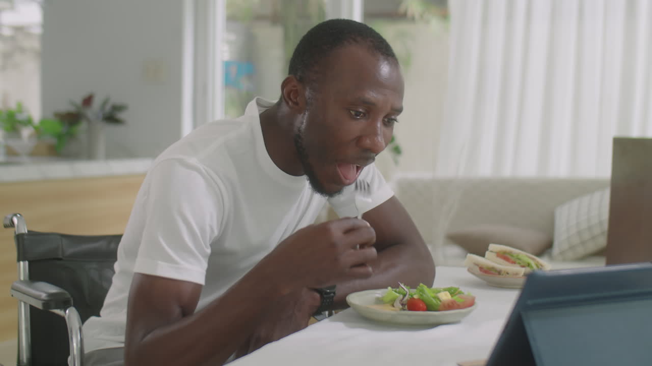 Black Man in Wheelchair Eating Meal and Using Tablet