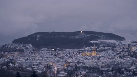 snow-covered town at twilight with hill and forest in the background
