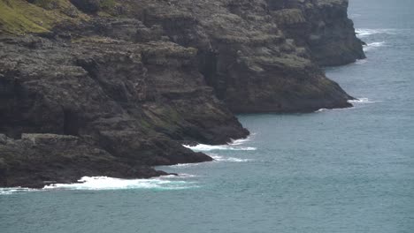 static wide shot showing waves crashing against rocky coastline of faroe islands