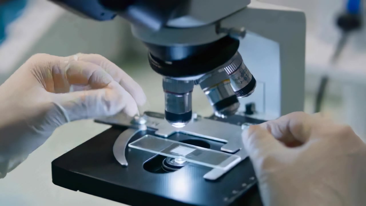Bringing gloved hands placing slide onto microscope stage, clipping ...