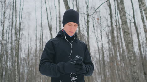 un joven con un martillo negro en invierno se prepara para correr en el parque, incluye una aplicación para correr y corre con un asistente de voz por el bosque haciendo negocios y llevando un estilo de vida saludable.