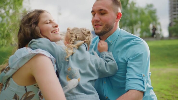 Un bambino gioioso corre in un parco soleggiato, ridendo con libertà. La famiglia condivide momenti teneri all'aperto, sorridendo e abbracciandosi. La scena cattura felicità, calore e una connessione naturale.