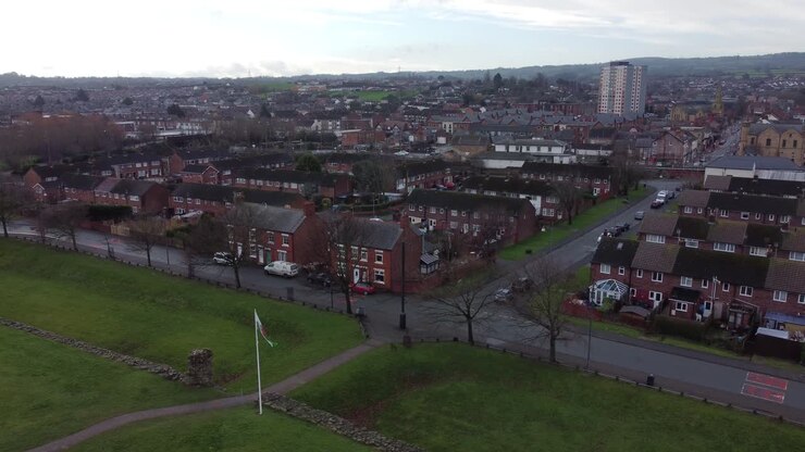 Bandiera gallese che sventola sul quartiere residenziale di Flint, strada cittadina suburbana, ripresa aerea del Galles del Nord, discesa lenta